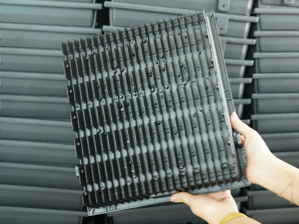 Hand holding the finned aluminum heat sink of an LED flood light module, showing the dense cooling fins on the back of the fixture