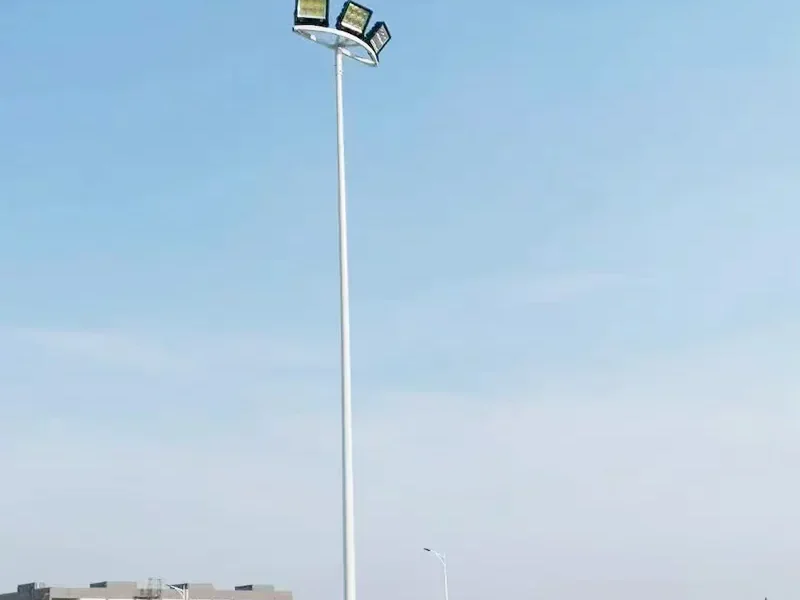 High mast lighting tower against an overcast sky, its crown carrying a ring of LED floodlights aimed outward