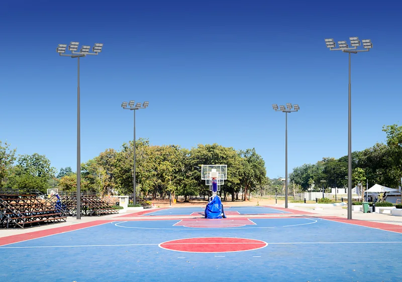 Blue and red outdoor multi-sport court surrounded by four floodlight masts carrying clusters of LED floodlights